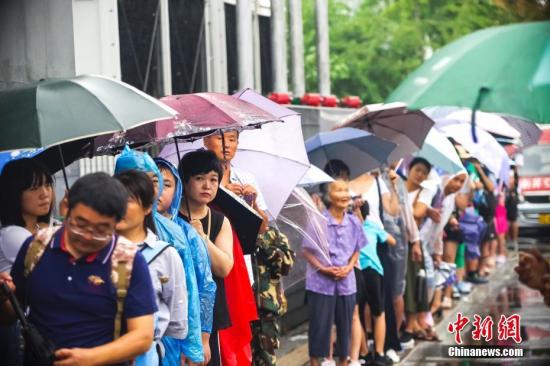 8月12日，游客冒雨在清华大学校门外排队等候入校参观。暑假以来，不少游客带着子女蜂拥至北京大学、清华大学等高校，一睹中国最高学府的风采。中新社记者贾天勇 摄